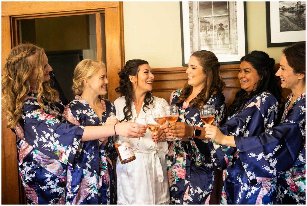 bridesmaids wear matching robes and cheers with wine before wedding