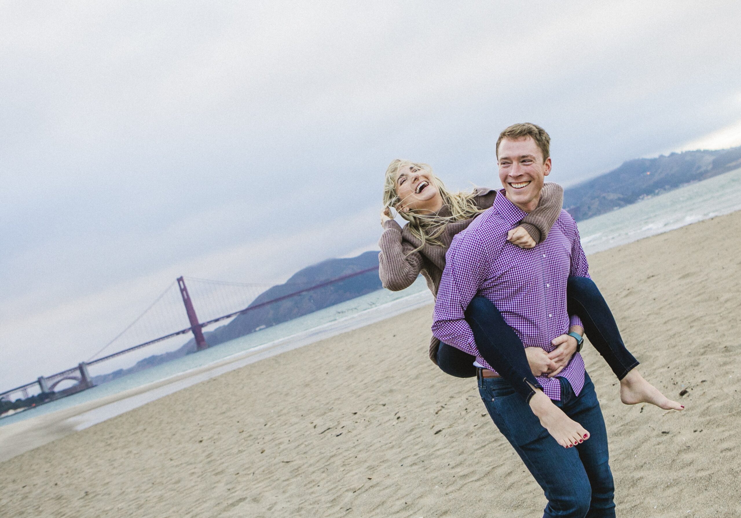 laughing couple on san francisco beach with golden gate bridge by Nightingale Photography