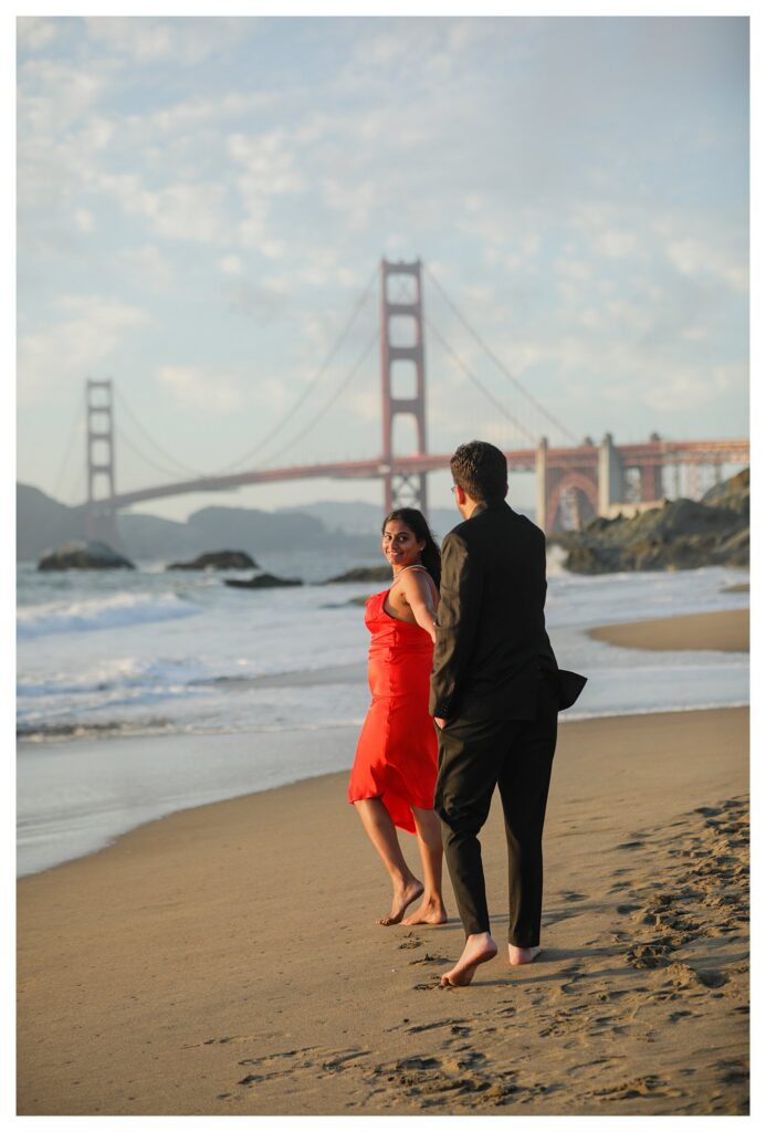 couple holds hands on baker beach for engagement pictures